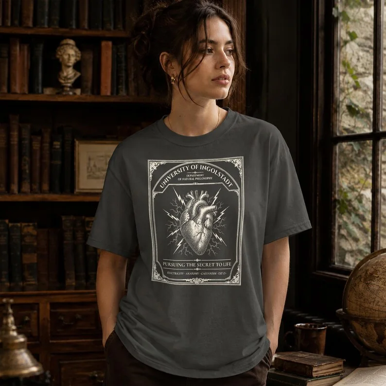 Pepper grey Comfort Colors Frankenstein University of Ingolstadt t-shirt worn by a man in a dark gothic library setting