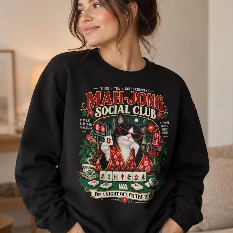 Woman wearing black Mah-Jong Social Club sweatshirt with cat, mahjong tiles, Hong Kong night scene and red, green and gold vintage artwork.