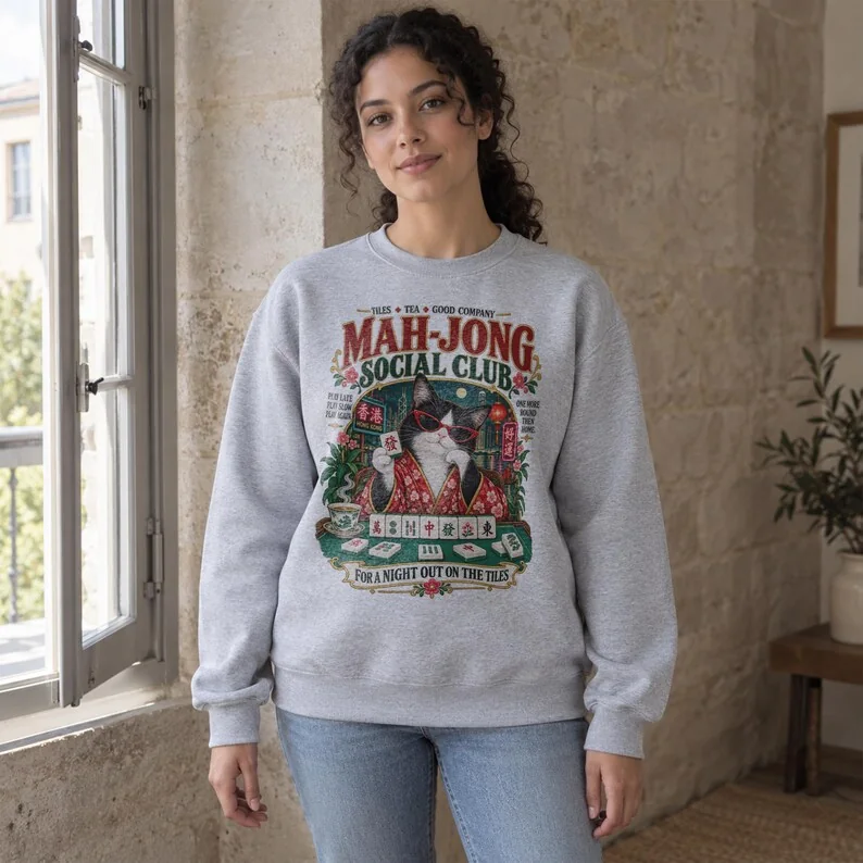 Woman wearing Sport Grey mahjong sweatshirt featuring the Mah-Jong Social Club cat design with tiles, lanterns and floral details.