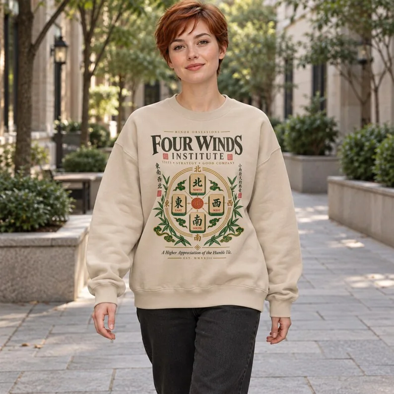 Woman wearing Sand Four Winds Institute sweatshirt with four mahjong wind tiles and vintage green, red and gold design.
