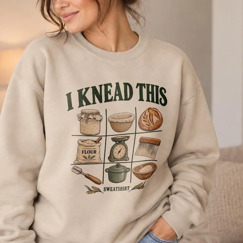 Woman wearing a sand Gildan 18000 crewneck sweatshirt with vintage I Knead This sourdough baking design.