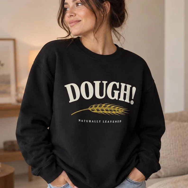 Black DOUGH sourdough sweatshirt on woman, with vintage bakery typography, golden wheat and Naturally Leavened design.